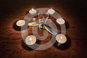 Power outage concept. An electric light bulb with a yellow-blue ribbon (the national symbol of Ukraine) in a circle of burning can
