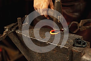 Close-up working powerful hands of male blacksmith forge an iron product in a blacksmith. Hammer, red hot metal and