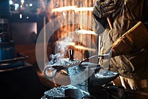 The blacksmith forging the molten metal on the anvil in smithy.