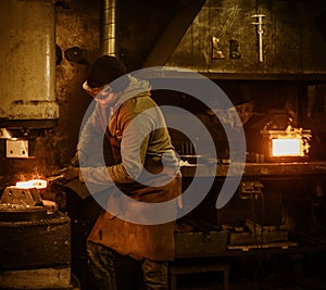 The blacksmith forging the molten metal on the power hammer in smithy