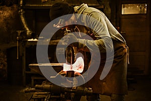 Blacksmith forging the molten metal on the rusty vise in smithy