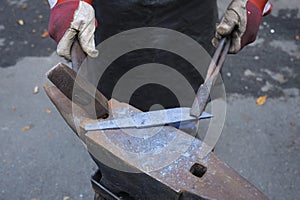 Blacksmith hands holding forceps and a hammer forging a metal billet, blade of a knife, on an anvil