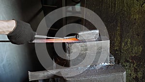Blacksmith holding candent iron ingot and forging it using pneumatic hammer.