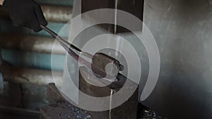 Blacksmith holding candent iron ingot and forging it using pneumatic hammer.