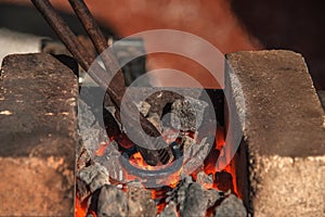 The blacksmith holds the tongs and heats the iron billet while the iron hotly creates a horseshoe on the anvil