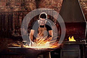 Blacksmith, man and metal workshop and sparks, manual forge working on hot steel with hammer, and fire. Worker, person