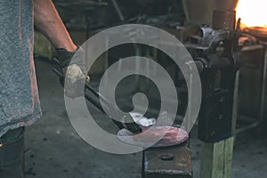 The blacksmith manually forging the molten metal on the anvil -