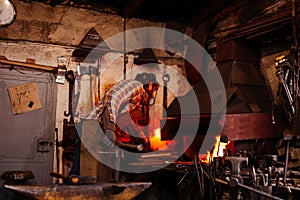 The blacksmith manually forging the molten metal on the anvil in smithy.