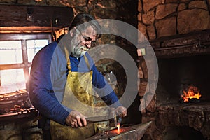 Blacksmith manually forging the molten metal on the anvil in smithy photo