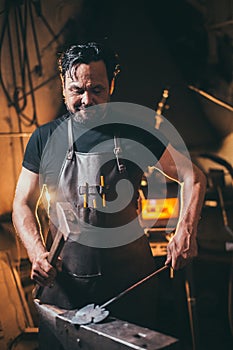 Blacksmith manually forging molten metal on anvil in smithy with spark fireworks