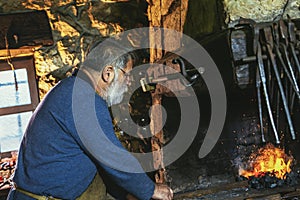 Blacksmith manually forging the molten metal on the anvil in smithy with spark fireworks