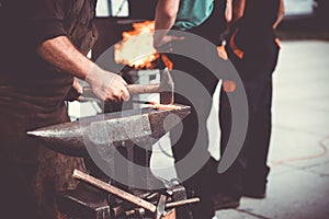 The blacksmith manually forging the molten metal on the anvil in smithy with spark fireworks, artwork