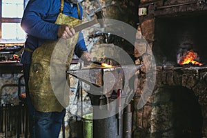 Blacksmith manually forging the molten metal on the anvil in smithy with spark fireworks, close up
