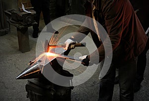 The blacksmith manually forging the molten metal on the anvil in smithy with spark fireworks. Spark. Dark background.