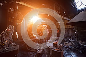 Blacksmith manually forging the molten metal with sunlight through the windows