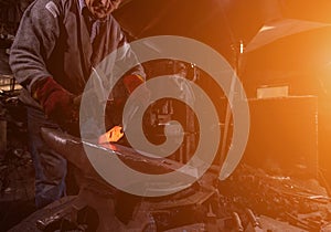 Blacksmith manually forging the molten metal with sunlight through the windows