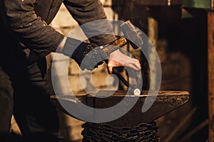 The blacksmith manually forging the red-hot metal on the anvil in smithy.