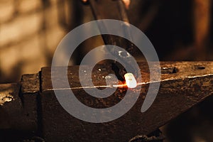 The blacksmith manually forging the red-hot metal on the anvil in smithy.