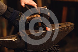 The blacksmith manually forging the red-hot metal on the anvil in smithy.