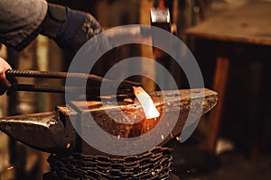 The blacksmith manually forging the red-hot metal on the anvil in smithy with spark fireworks.