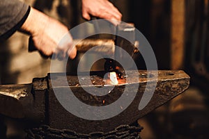 The blacksmith manually forging the red-hot metal on the anvil in smithy with spark fireworks.