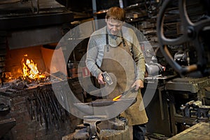 The blacksmith manually forging the red-hot metal on the anvil in smithy with spark fireworks