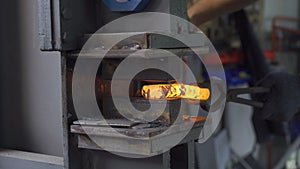 Blacksmith nipping a hot metal rod by machine