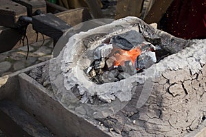 Blacksmith sets up the brazier with embers with large coal tongs. Embers glow in a iron forge. Fire, heat, coal and ash