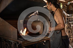 Blacksmith stoking the fire in the forge of his workshop