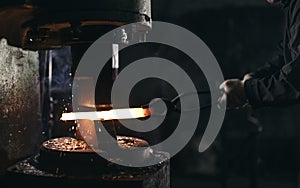 Blacksmith using hydraulic press for steel arms manufacture at smithy workshop