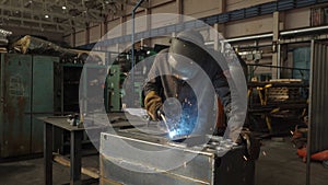 Blacksmith welder in protective mask works with metal using a welding machine