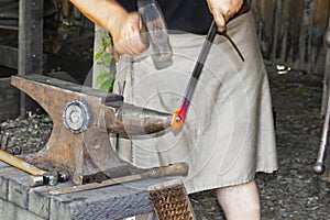 Blacksmith in a work kilt pounding a red hot piece of metal with a hammer on an anvil - hands in motion