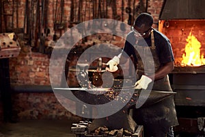 Blacksmith, worker and metal forge in workshop and manual industry working on hot steel with hammer, sparks or fire