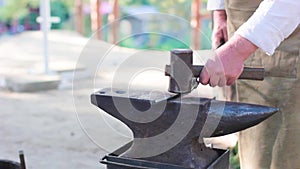 Blacksmith working with an iron details in his workshop - hitting the metal piece with a hammer, bending it