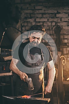 Blacksmith working metal with hammer on anvil in the forge