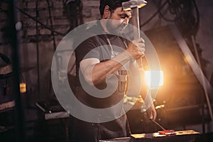 Blacksmith working metal with hammer on anvil in the forge