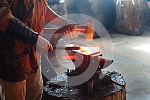 Blacksmith working metal with hammer on the anvil in the forge