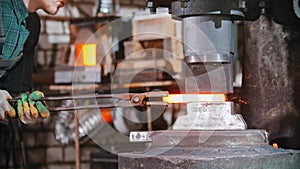 Blacksmith working - putting a longer piece of metal under the pressure of industrial forging machine