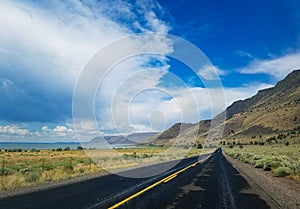 Blacktopped road running between volcanic mountains and a lake with a big blue sky photo