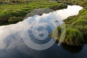 Blackwater marsh and river with grassy hillocks and reflections of white clouds