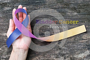 Bladder cancer awareness marigold blue purple  ribbon color splashed on helping hand, old aged background