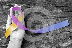 Bladder cancer awareness marigold blue purple ribbon on helping hand suport isolated with clipping path