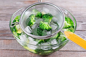 Blanched broccoli cabbage florets in a sieve in icy water on wooden table