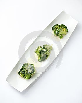 Blanched broccoli with sauce, mini portion. Vegetables on white plate. Diet food, minimum calories. Object isolated on