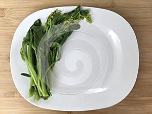 Blanched vegetable are placed on the left side of board on a white plate on a brown wooden.