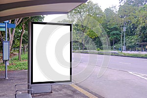 _Blank advertising poster banner mockup template at empty bus stop shelter by main road. Greenery around vertical out-of-home OOH