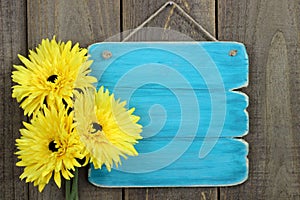 Blank antique blue sign with large yellow sunflowers hanging on rustic wood fence