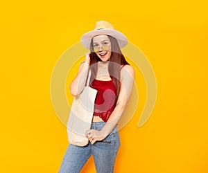 Blank beach or shopping eco bag in hands of smiling young girl in hat and yellow glasses standing over yellow background. Summer,