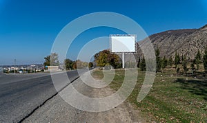 Blank billboard sign by empty highway through mountains landscape.