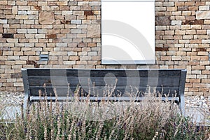 Blank billboard on a stone wall and a banch in front and a dry grass